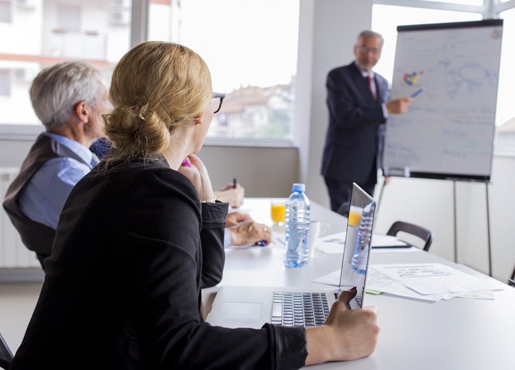 businesspeople-looking-man-giving-presentation-flip-chart